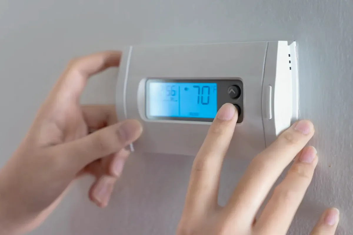 Hands adjusting a digital wall thermostat